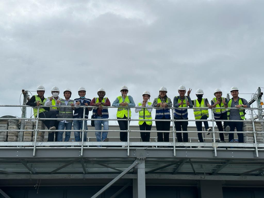 Group of construction workers in high-visibility vests and hard hats standing on a platform with a cloudy sky in the background.